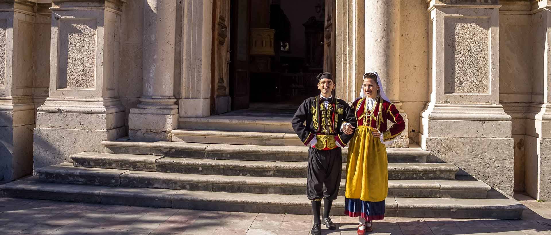 A local man and woman standing in front of Prčanj Temple during a private tour, dressed in traditional Boka bay clothes. The entrance to Prčanj Temple is also visible.